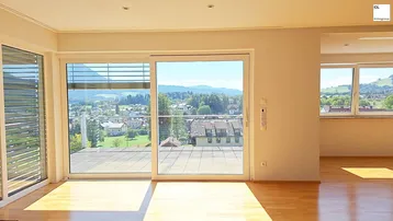 Helles Wohnzimmer mit großen Schiebetüren, die auf eine weitläufige Terrasse führen und einen weiten Blick bieten.