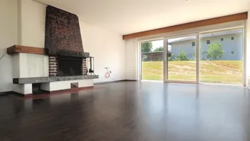 Geräumiges Wohnzimmer mit großem Kamin, dunklem Parkettboden und Zugang zum Garten.