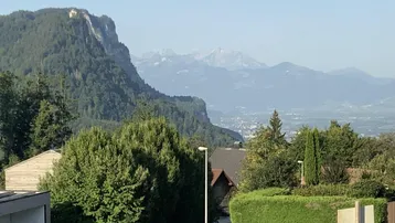 Weitläufiger Blick über grüne Hügel und eine Stadt in der Ferne, umgeben von Bergen.