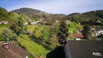 Panoramablick über eine grüne Hügellandschaft mit verstreuten Häusern unter blauem Himmel.
