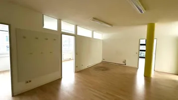 Heller Büroraum mit Holzfußboden, weißen Wänden und einem auffälligen gelben Pfeiler in der Mitte.