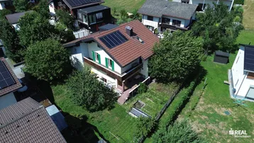 Luftaufnahme des Hauses mit Solaranlage auf dem Dach und umliegender grüner Landschaft.