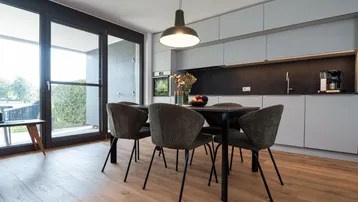 Moderner offener Wohn-Essbereich mit integrierter Küche, Holzboden und Zugang zur Terrasse.