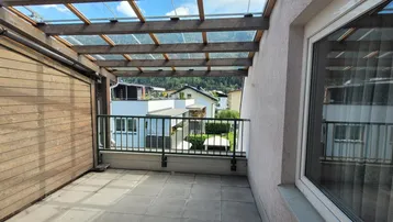 Überdachter Balkon mit Holzwänden und Blick auf die umliegenden Häuser und Berge.