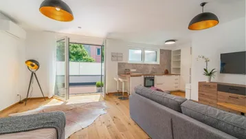 Heller offener Wohnbereich mit integrierter Küche, Holzboden und Zugang zu einer Terrasse.