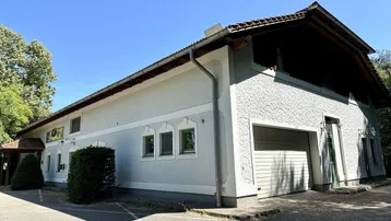Ansicht des Gebäudes von der Seite mit Parkplätzen und grüner Umgebung unter blauem Himmel.