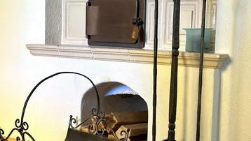 Detailansicht des traditionellen Kachelofens mit schmiedeeisernem Kaminbesteck und Holzscheiten.
