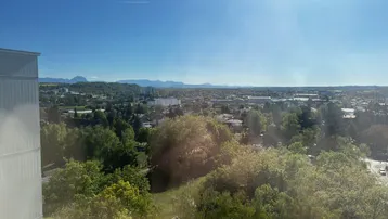 Weitläufiger Ausblick über die Stadt und die umliegende grüne Landschaft mit Bergen am Horizont.