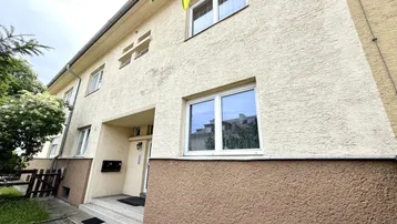Vorderansicht eines Reihenhauses mit beiger Fassade und braunem Sockelbereich unter hellem Himmel.