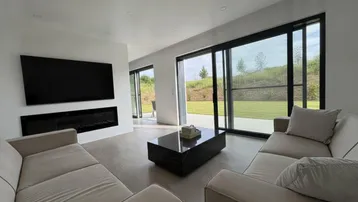 Helles Wohnzimmer mit integriertem Kamin, Fernseher und weitem Blick ins Grüne.