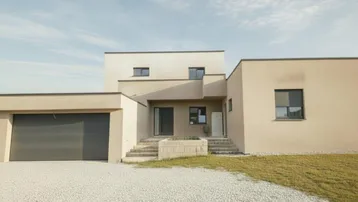 Moderne Hausfassade mit integrierter Garage und Kiesauffahrt unter hellem Himmel.
