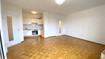 Helles Wohnzimmer mit integrierter Küchenzeile und Parkettboden.