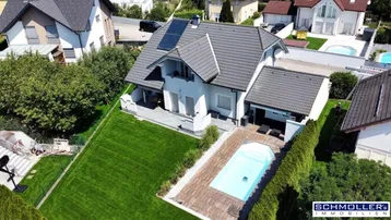 Luftaufnahme eines Einfamilienhauses mit großem Garten, Swimmingpool und Photovoltaikanlage auf dem Dach.