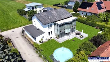 Luftaufnahme eines modernen Hauses mit Glasfassade, großem Garten und Pool in ländlicher Umgebung.