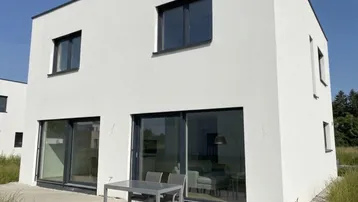 Moderne weiße Hausfassade mit großen Fenstern und einer möblierten Terrasse im Freien.
