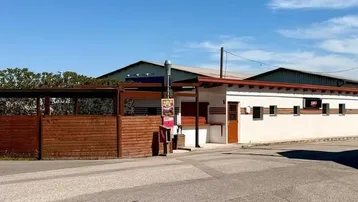 Gebäudeansicht eines Gewerbeobjekts mit weißer Fassade und angrenzender Holzverkleidung im Außenbereich.