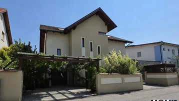 Modernes Einfamilienhaus mit Satteldach, Carport und gepflegter Vorgartengestaltung unter blauem Himmel.