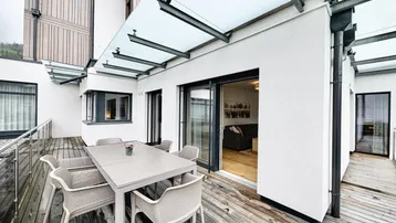 Geräumige Terrasse mit Holzboden, Esstisch und Glasüberdachung, ideal für Mahlzeiten im Freien.