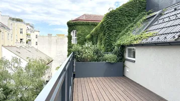 Geräumige Dachterrasse mit Holzboden, Pflanzen und Blick auf die umliegenden Gebäude.