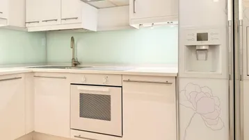 Moderne weiße Küche mit integrierten Geräten, Dunstabzugshaube und floralem Kühlschrankdesign.