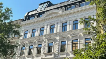 Elegante Fassade eines Altbaus mit reich verzierten Stuckelementen und modernen Dachgauben unter blauem Himmel.