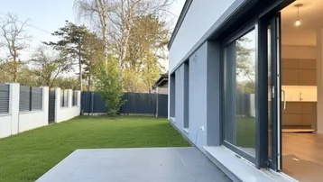 Moderne Terrasse mit Fliesenboden und Zugang zum Garten, daneben ein Blick in die Küche.