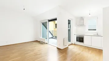 Heller Wohn- und Essbereich mit Parkettboden, Zugang zum Balkon und integrierter Küchenzeile.