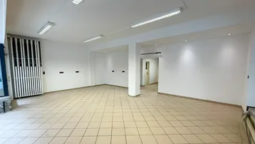 Geräumiger, leerer Gewerberaum mit hellen Fliesenböden und moderner Deckenbeleuchtung, ideal für ein Geschäft.