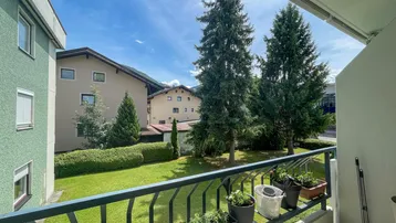 Heller Balkon mit Blick auf eine gepflegte Grünfläche und umliegende Wohnhäuser an einem sonnigen Tag.