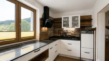 Moderne Küche mit weißen Fronten, Steinarbeitsplatte und Blick ins Grüne durch das Fenster.