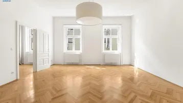 Helles Wohnzimmer mit Fischgrätparkettboden, hohen Decken und zwei großen Fenstern.