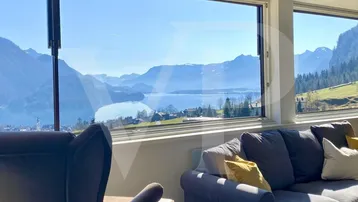 Helles Wohnzimmer mit großen Fenstern und atemberaubendem Blick auf den See und die Berge.