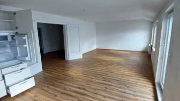 Geräumiger, heller Raum mit Holzfußboden und großen Fenstern, ideal für Wohn- und Essbereich.