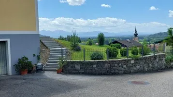 Blick auf die Seitenfassade des Hauses mit Steintreppe und weitem Ausblick auf die Landschaft und Berge.