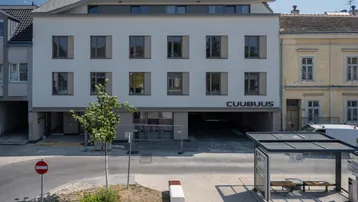 Neubau mit heller Fassade, großen Fenstern und integrierter Tiefgaragenzufahrt an einer städtischen Straße.