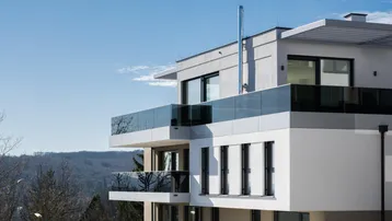 Ansicht der modernen Wohnanlage mit gestuften Balkonen, Glasgeländern und weitem Blick in die Landschaft.