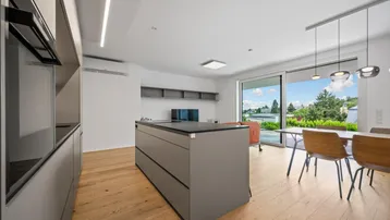 Moderne offene Küche mit Kochinsel, Essbereich und Zugang zur Terrasse.