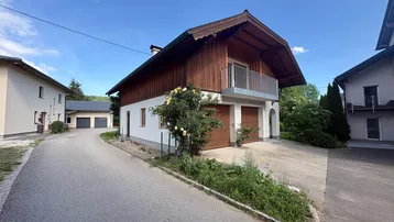 Traditionelles Haus mit Holzfassade, zwei Garagen und einem kleinen Balkon unter blauem Himmel.