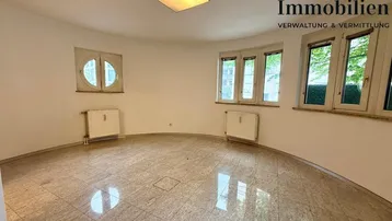 Geräumiger, leerer Raum mit Fliesenboden, gebogener Wand und mehreren Fenstern, ideal als Wohnzimmer.