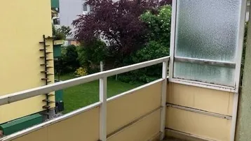 Balkon mit Fliesenboden, gelbem Geländer und Blick ins Grüne sowie auf umliegende Gebäude.