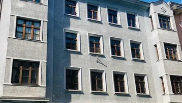 Graue Fassade eines Mehrfamilienhauses mit vielen Fenstern unter blauem Himmel.