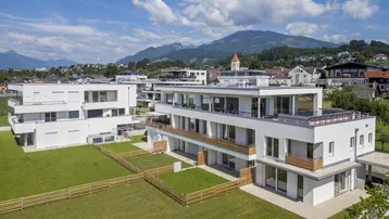 Moderne Wohngebäude mit weitläufigen Grünflächen und Bergblick unter blauem Himmel.
