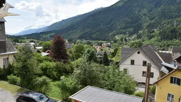 Weitläufiger Blick auf die umliegende Berglandschaft und das Tal mit Häusern.