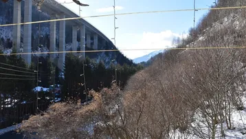Panoramablick von einem Balkon auf eine beeindruckende Brücke, Berge und eine verschneite Landschaft.