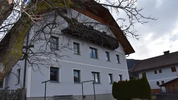 Traditionelles Wohnhaus mit heller Fassade, umgeben von einem kleinen Vorgarten und altem Baumbestand.