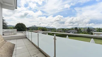 Geräumige Terrasse mit Glasgeländer und Panoramablick auf die umliegende Berglandschaft.