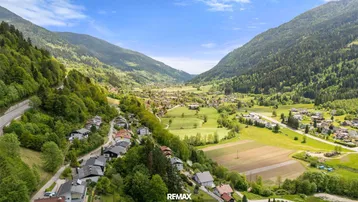 Weitläufige Luftaufnahme des Tals mit Siedlungen, Feldern und bewaldeten Bergen.