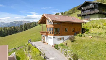 Traditionelles Holzhaus in alpiner Landschaft mit Bergblick und integrierter Garage.