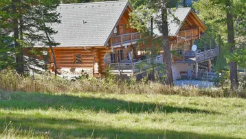 Rustikales Holzhaus im Blockhausstil, umgeben von Bäumen und einer grünen Wiese.