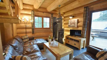 Gemütliches Wohnzimmer im Blockhausstil mit Ledersofas, Kaminofen und Zugang zur Terrasse.